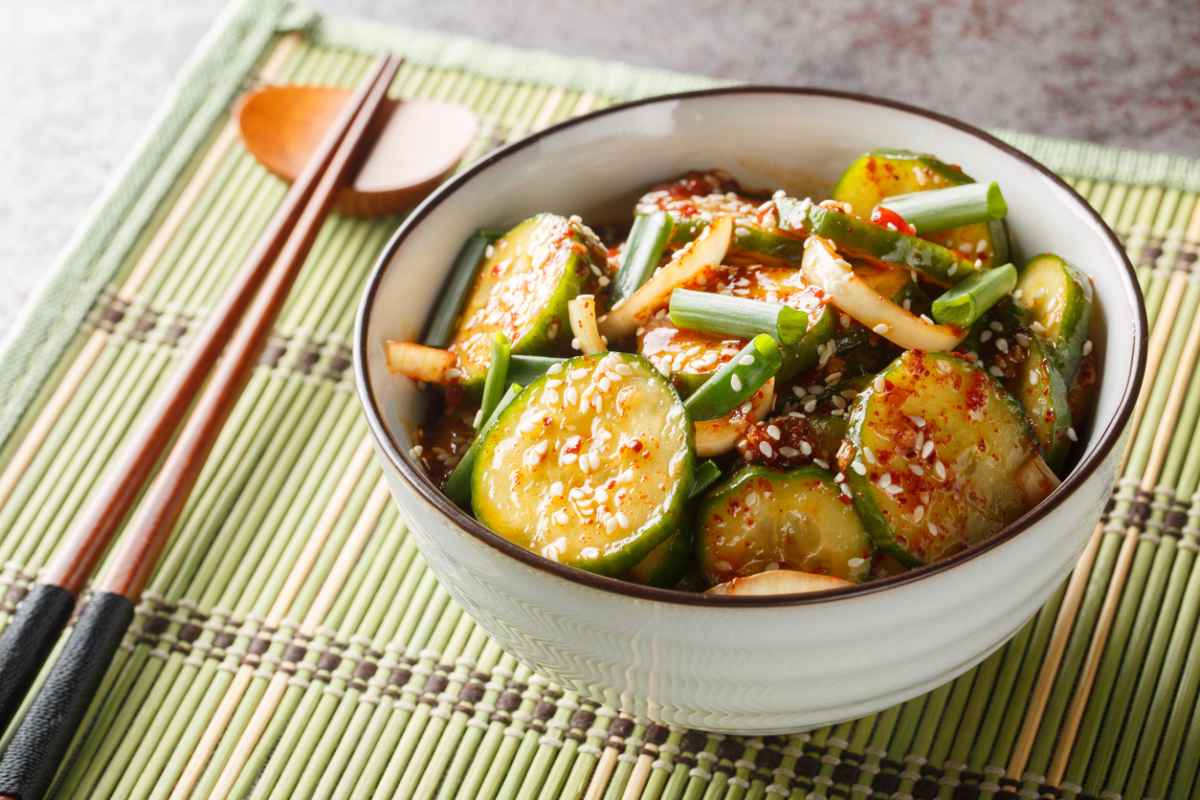 Dubenyje yra agurkų salotos su svogūnais, žaliosiomis žolelėmis ir sezamo sėklomis.